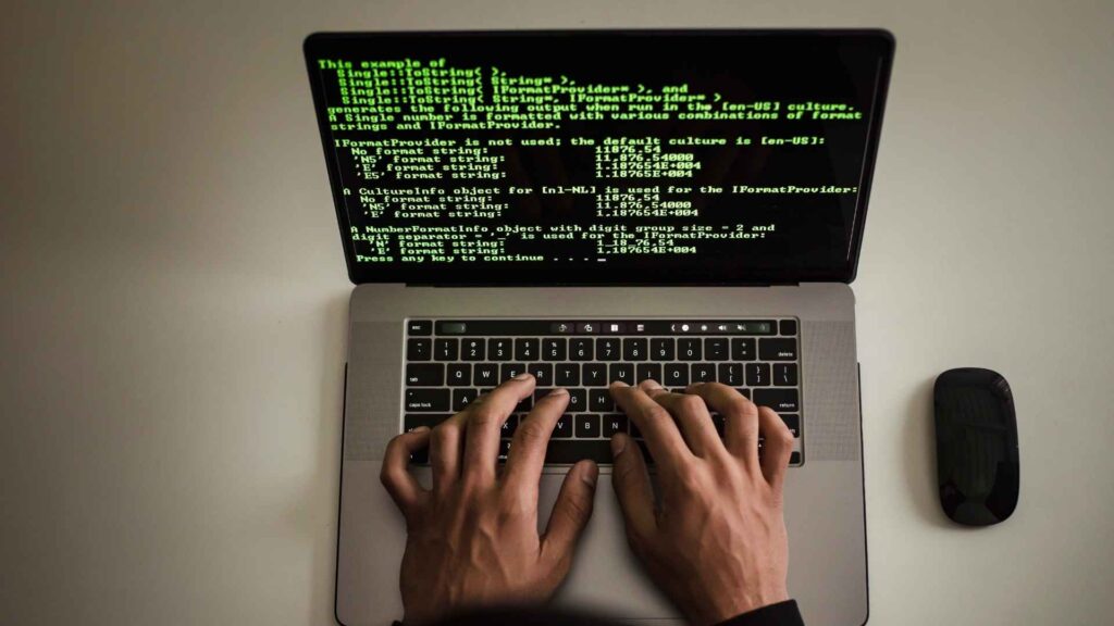 pessoa digitando em um notebook com tela exibindo código de programação em fundo preto.