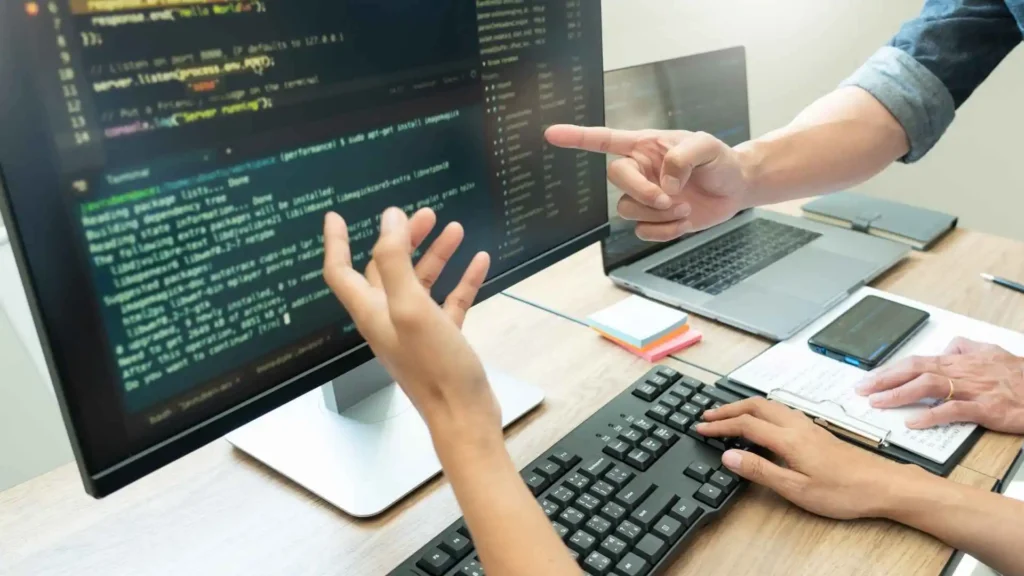 Mãos de duas pessoas discutem pontos de melhoria em programação iniciante.