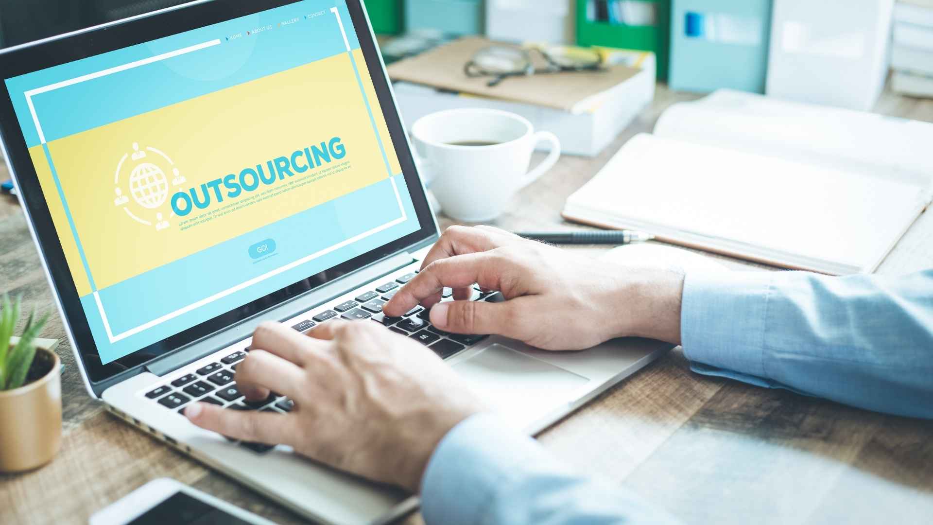 Pessoa digitando em um notebook com a palavra "Outsourcing" na tela.