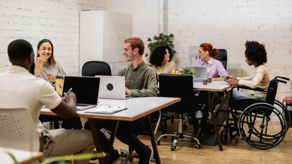 Equipe diversa trabalhando em ambiente de tecnologia com inclusão, mostrando pessoas de diferentes perfis e uma profissional em cadeira de rodas