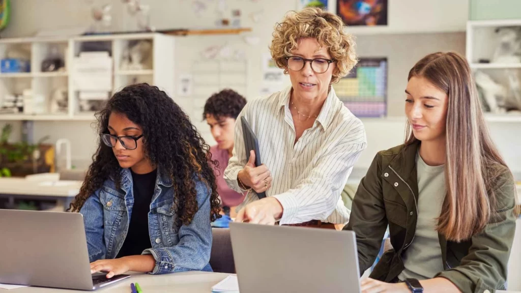 Instrutora auxiliando alunos em um bootcamp de tecnologia com foco em programação e prática de mercado